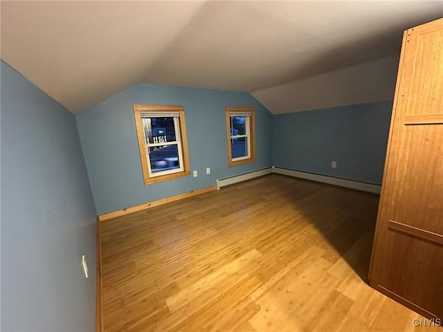 additional living space featuring light wood-type flooring, a baseboard radiator, and vaulted ceiling