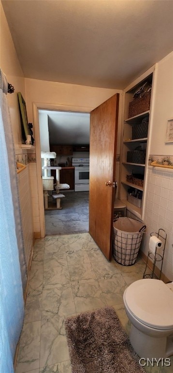 bathroom with toilet, a wainscoted wall, and tile walls