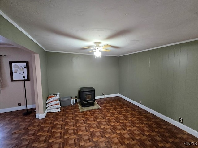 unfurnished room with ornamental molding, a wood stove, baseboards, and a ceiling fan