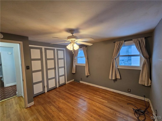 unfurnished bedroom with ceiling fan, wood finished floors, visible vents, and baseboards