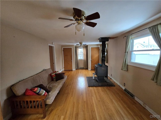 unfurnished living room with visible vents, light wood-style floors, a ceiling fan, a wood stove, and baseboards