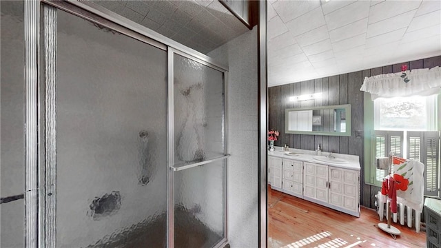 bathroom featuring hardwood / wood-style floors, vanity, a shower with door, and wooden walls