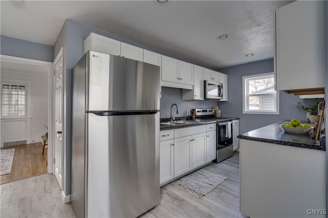 kitchen with a textured ceiling, stainless steel appliances, sink, white cabinets, and light hardwood / wood-style floors