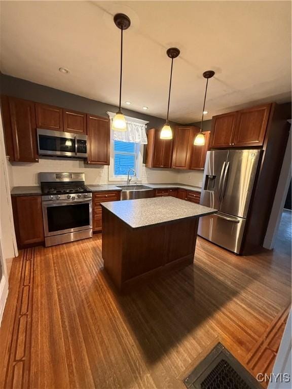 kitchen with dark hardwood / wood-style flooring, stainless steel appliances, sink, a kitchen island, and hanging light fixtures