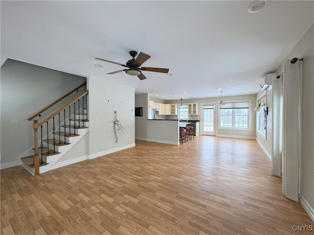 unfurnished living room with a wall mounted AC, light hardwood / wood-style flooring, and ceiling fan