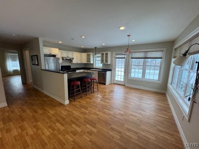 kitchen with appliances with stainless steel finishes, light hardwood / wood-style flooring, white cabinets, a kitchen island, and hanging light fixtures