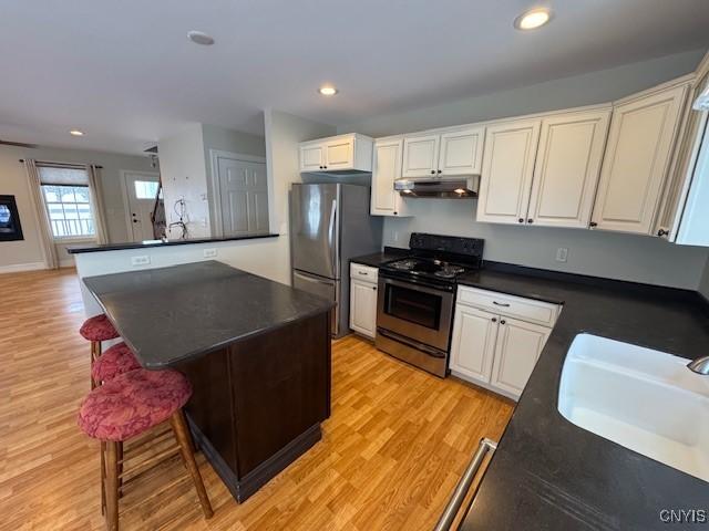 kitchen with white cabinets, a kitchen breakfast bar, sink, light hardwood / wood-style flooring, and stainless steel appliances