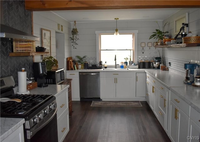 kitchen featuring backsplash, stainless steel appliances, wall chimney range hood, white cabinetry, and hanging light fixtures