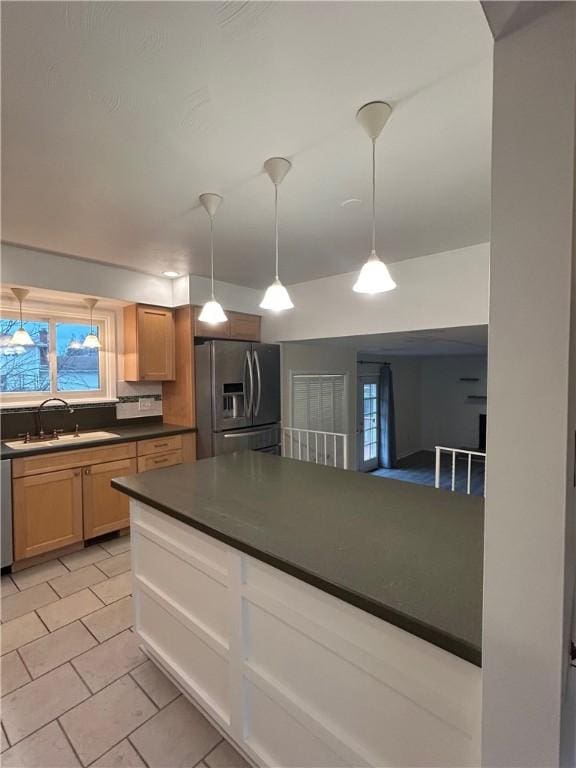 kitchen with appliances with stainless steel finishes, light brown cabinetry, sink, light tile patterned floors, and decorative light fixtures