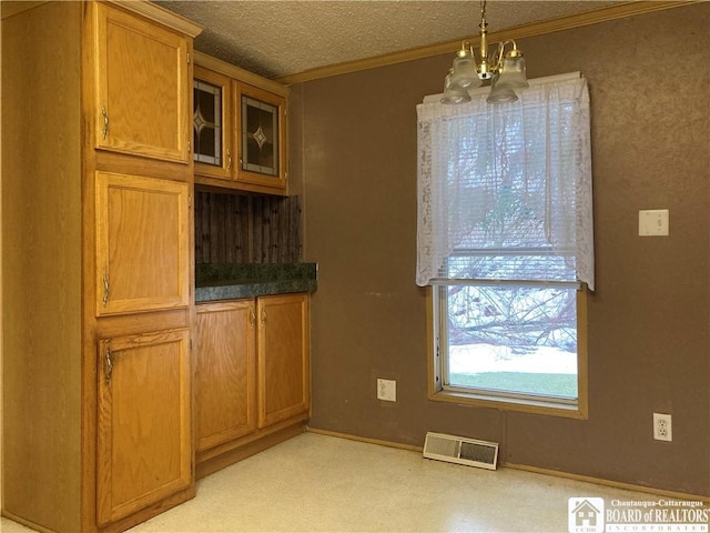 unfurnished dining area with a textured ceiling, crown molding, and a notable chandelier