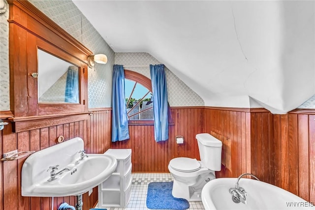 bathroom featuring a tub to relax in, vaulted ceiling, sink, toilet, and wood walls