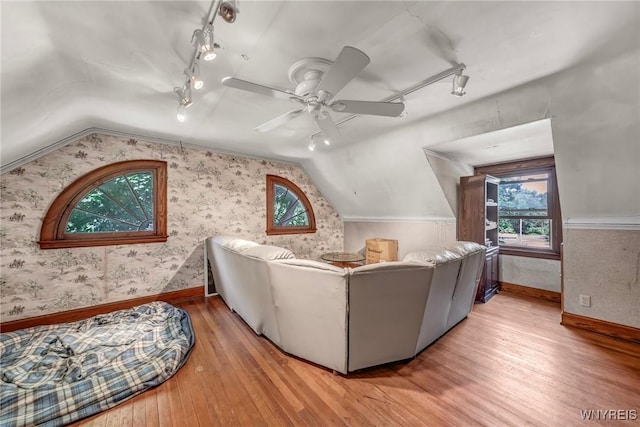 living room with ceiling fan, rail lighting, wood-type flooring, and lofted ceiling