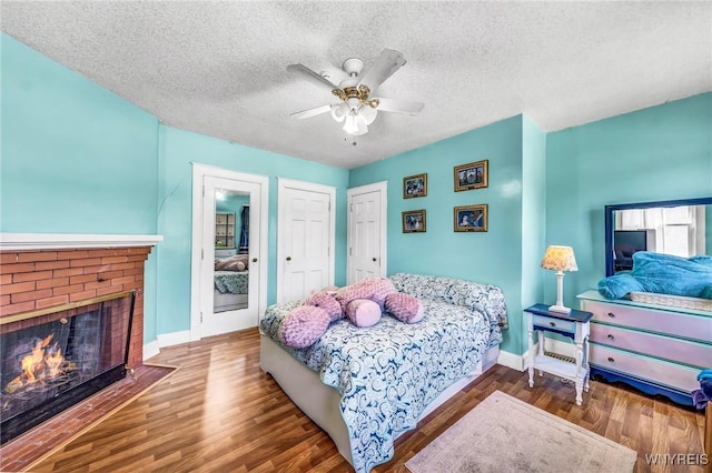 bedroom featuring ceiling fan, hardwood / wood-style floors, a textured ceiling, and a brick fireplace