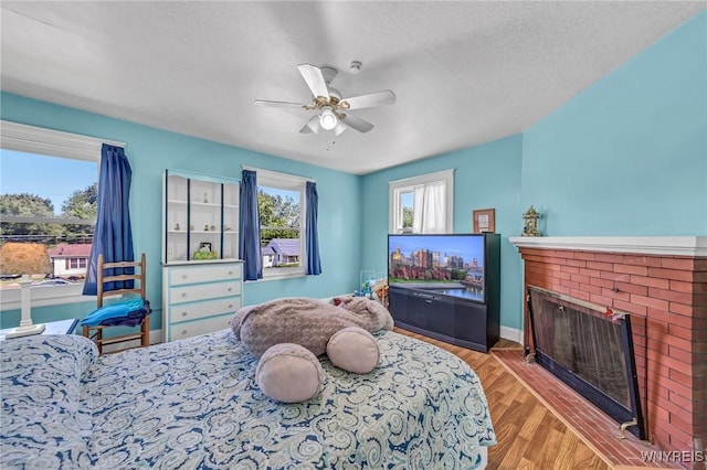 bedroom featuring ceiling fan, light wood-type flooring, a textured ceiling, and a brick fireplace