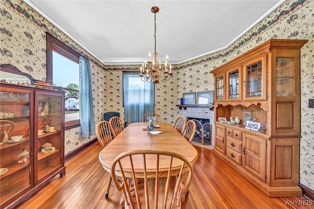 dining space featuring crown molding, light hardwood / wood-style flooring, a textured ceiling, and a notable chandelier