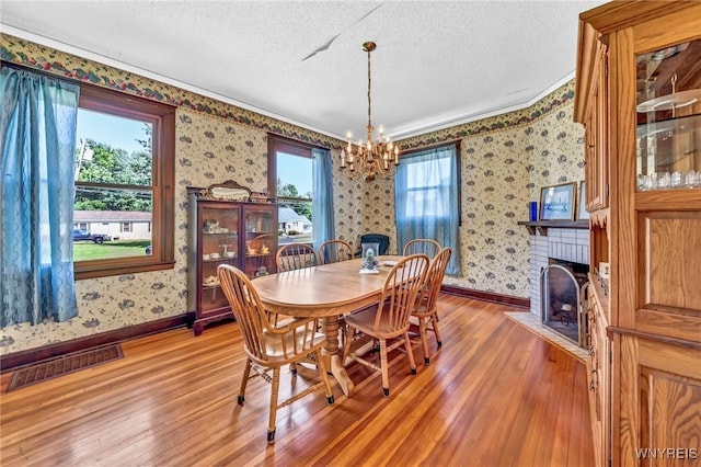 dining room with an inviting chandelier, wood-type flooring, a textured ceiling, and a brick fireplace