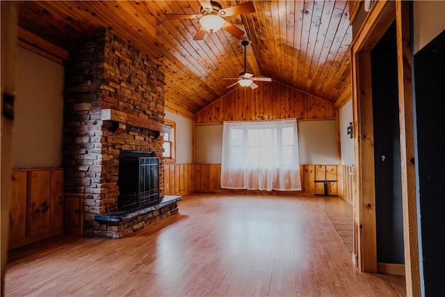 unfurnished living room featuring ceiling fan, wooden ceiling, a stone fireplace, light hardwood / wood-style floors, and vaulted ceiling