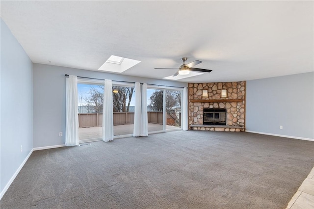 unfurnished living room featuring a stone fireplace, ceiling fan, carpet, and a skylight