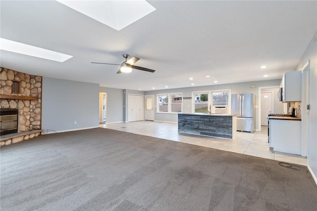 unfurnished living room with ceiling fan, light colored carpet, a fireplace, and a skylight