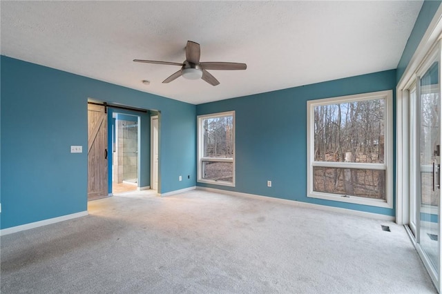 unfurnished bedroom featuring connected bathroom, ceiling fan, a barn door, carpet floors, and a textured ceiling