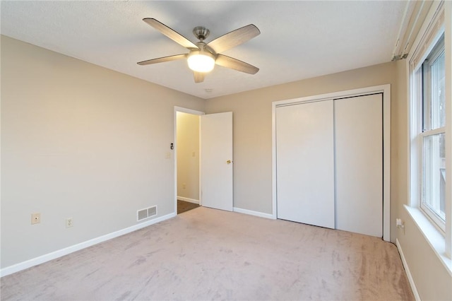 unfurnished bedroom featuring ceiling fan, light colored carpet, and a closet