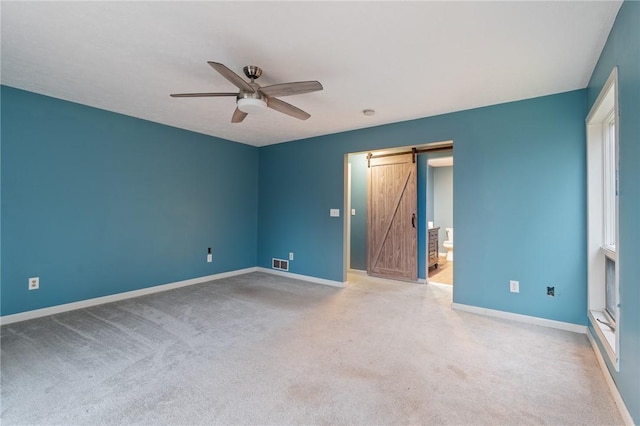 unfurnished bedroom featuring ceiling fan, a barn door, ensuite bathroom, and light carpet