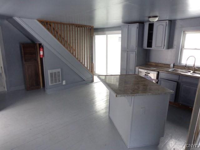 kitchen with gray cabinetry, dishwasher, sink, a center island, and light wood-type flooring