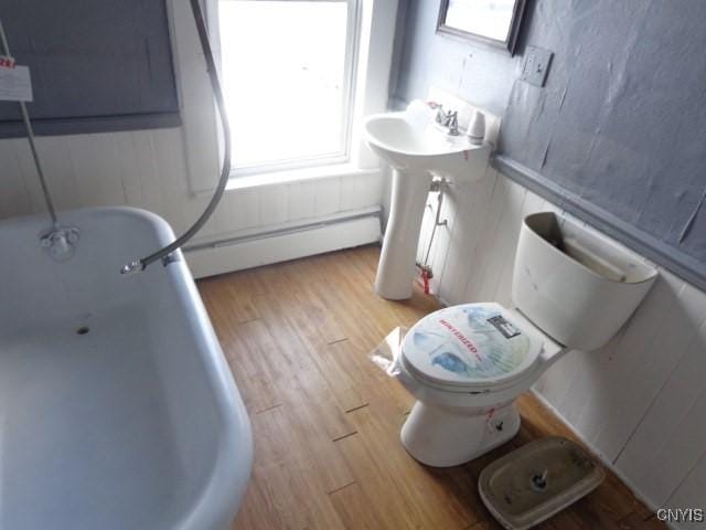 bathroom with hardwood / wood-style floors, a bathtub, toilet, and a baseboard heating unit