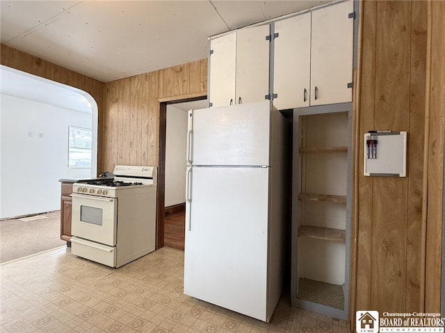 kitchen featuring wood walls, white cabinets, and white appliances