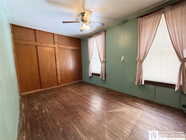 unfurnished bedroom with wooden walls, a closet, ceiling fan, and hardwood / wood-style flooring