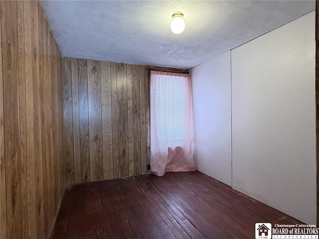 spare room with dark hardwood / wood-style flooring, a textured ceiling, and wooden walls