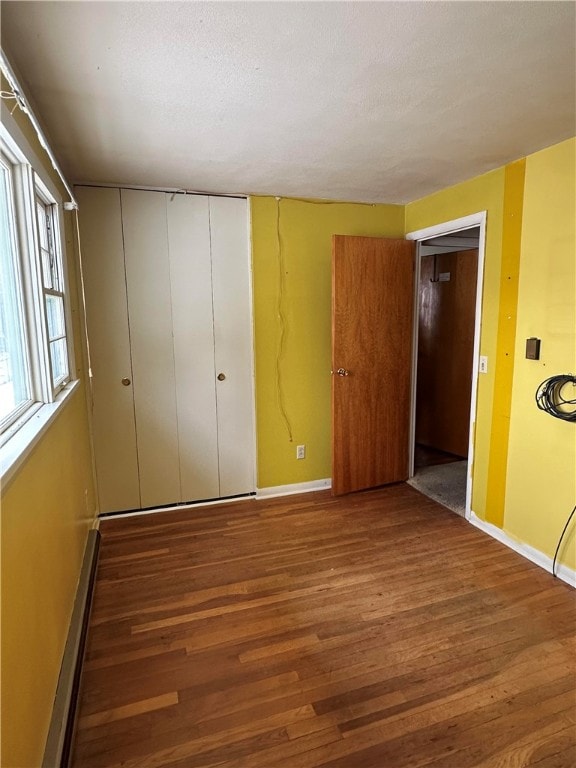 unfurnished bedroom featuring wood-type flooring, a closet, and a baseboard heating unit