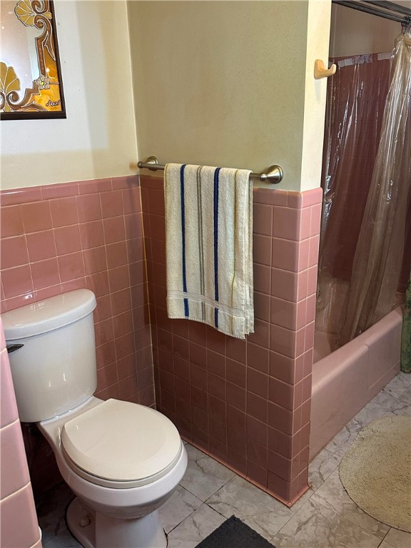 bathroom with shower / bathtub combination with curtain, toilet, and tile walls