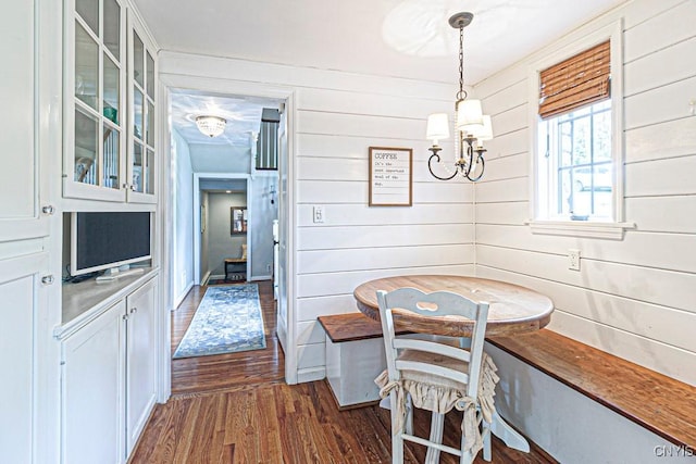 dining area featuring breakfast area, dark wood-type flooring, wooden walls, and a chandelier