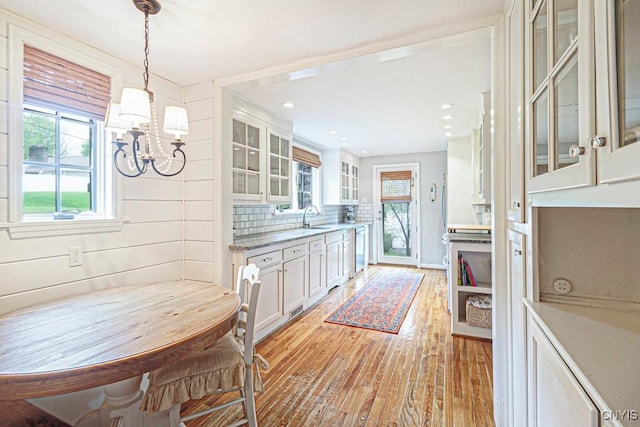 kitchen with stainless steel dishwasher, light stone counters, sink, pendant lighting, and white cabinetry