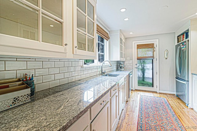 kitchen featuring decorative backsplash, appliances with stainless steel finishes, light wood-type flooring, light stone counters, and sink