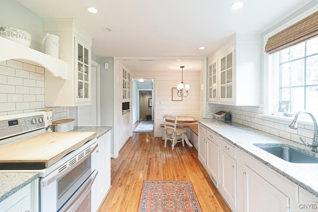 kitchen featuring white cabinets, sink, hanging light fixtures, and electric stove