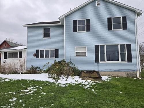 snow covered back of property featuring a lawn