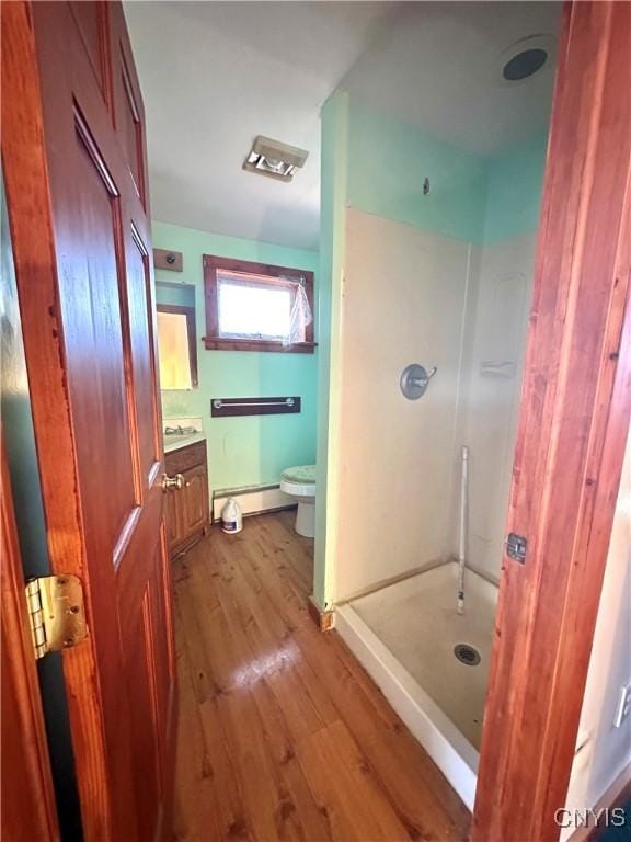 bathroom with a baseboard radiator, a shower, wood-type flooring, toilet, and vanity