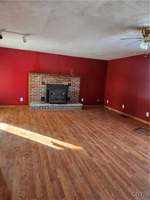 unfurnished living room featuring rail lighting, a brick fireplace, a textured ceiling, ceiling fan, and wood-type flooring