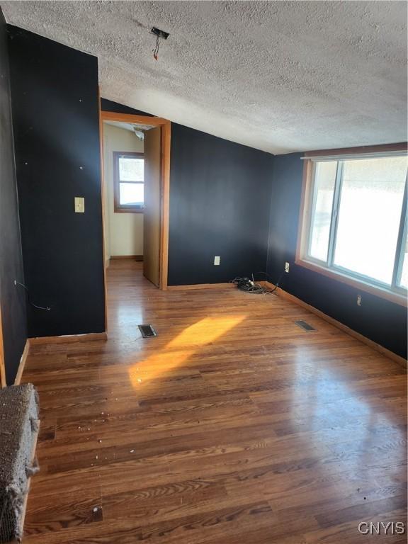 empty room with wood-type flooring, a textured ceiling, and vaulted ceiling