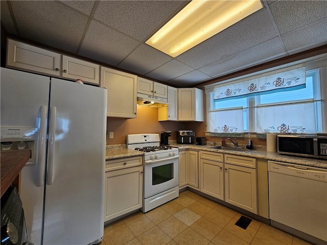 kitchen with light stone countertops, white appliances, a paneled ceiling, and sink