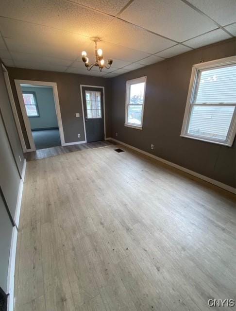 unfurnished dining area with a paneled ceiling, wood-type flooring, and a notable chandelier