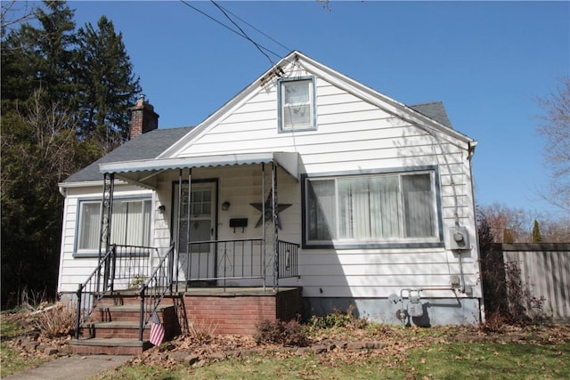 bungalow featuring a shingled roof, covered porch, fence, and a chimney