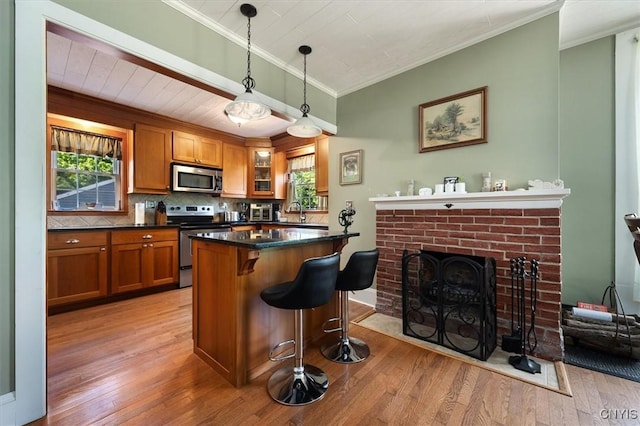 kitchen with a kitchen breakfast bar, hanging light fixtures, a brick fireplace, light wood-type flooring, and appliances with stainless steel finishes