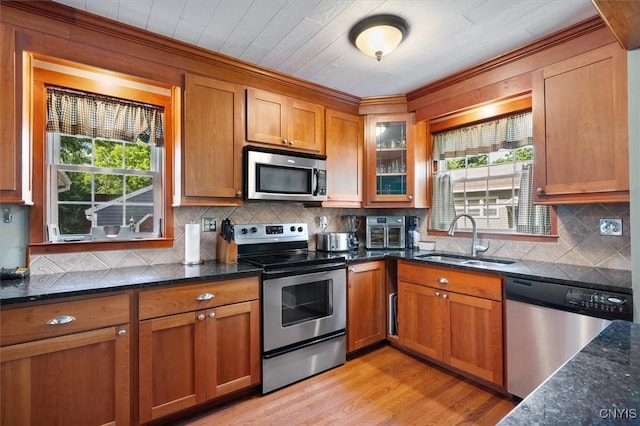 kitchen with sink, stainless steel appliances, backsplash, dark stone countertops, and light hardwood / wood-style floors