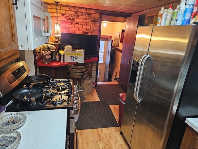 kitchen with hanging light fixtures, brick wall, white appliances, a paneled ceiling, and light wood-type flooring