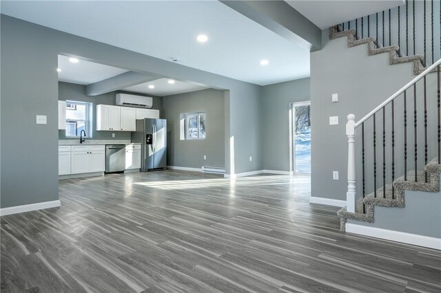 unfurnished living room with baseboard heating, a wall mounted AC, dark hardwood / wood-style flooring, and sink