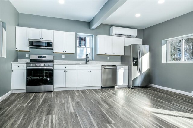 kitchen with stainless steel appliances, sink, an AC wall unit, white cabinets, and dark hardwood / wood-style floors