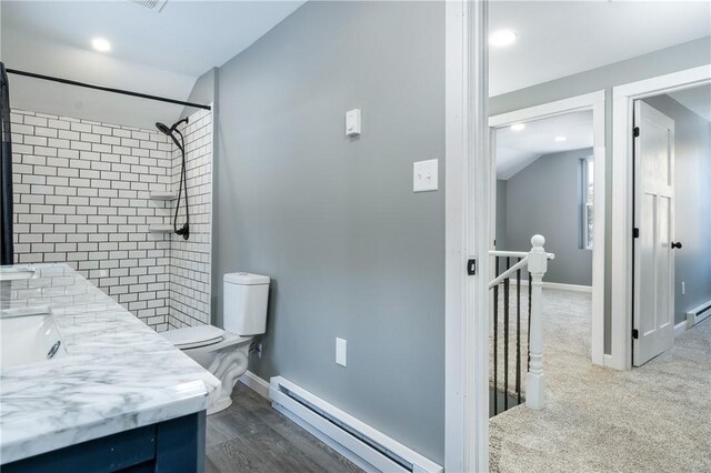 bathroom with a tile shower, vanity, a baseboard heating unit, toilet, and lofted ceiling